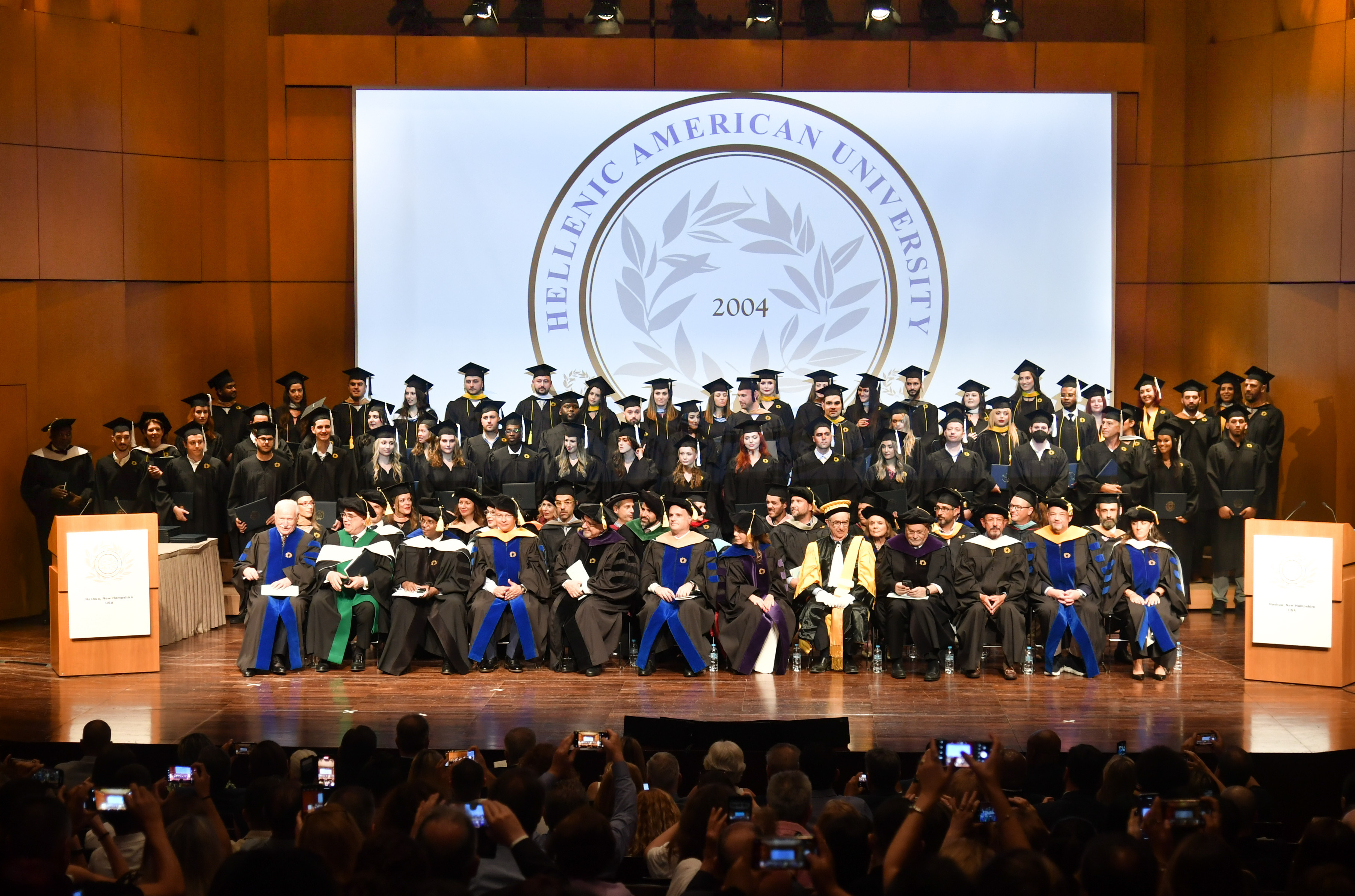 Group photo of Hellenic American University graduates (class of 2004) on stage of the amphitheatre.